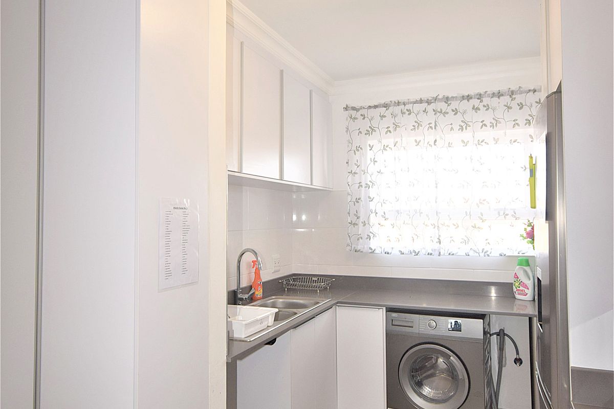 A functional laundry area featuring built-in white cabinetry, a stainless steel sink, tiled flooring, and space for a washing machine.