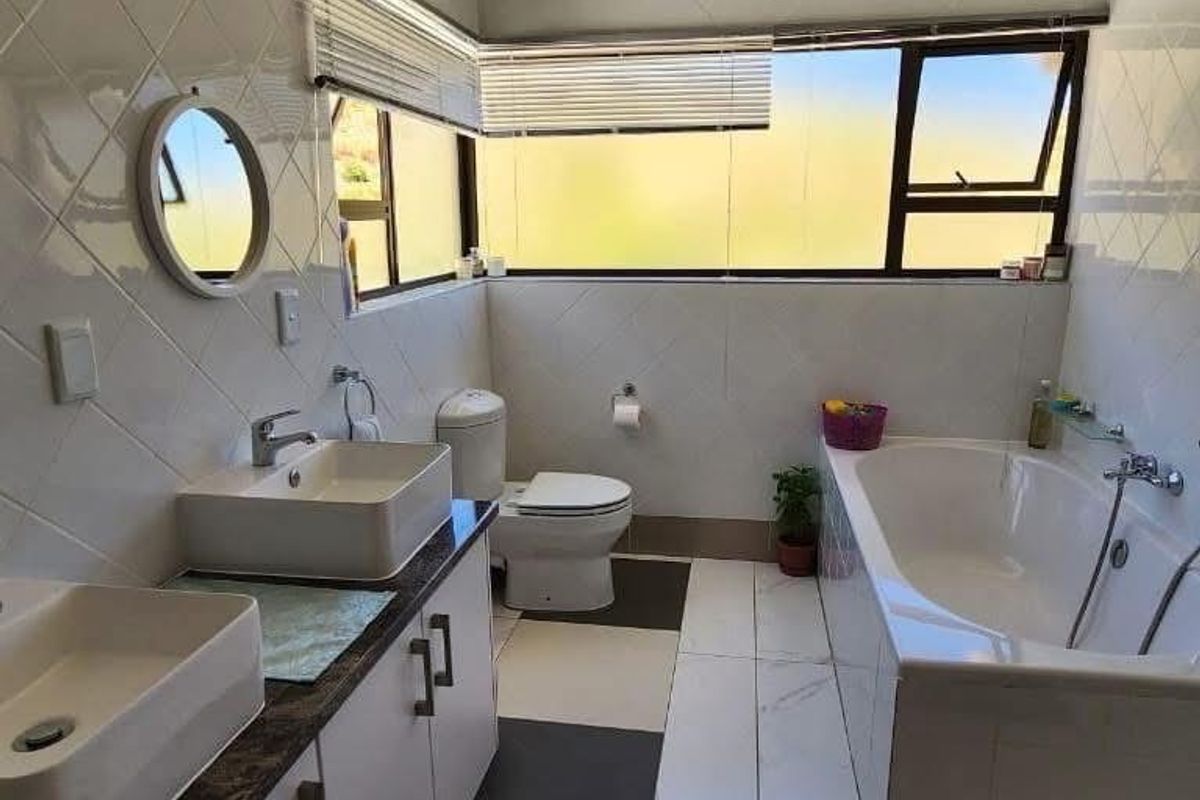 A functional bathroom featuring dual vessel sinks on a vanity, a built-in bathtub, and a toilet with tiled walls and floors.