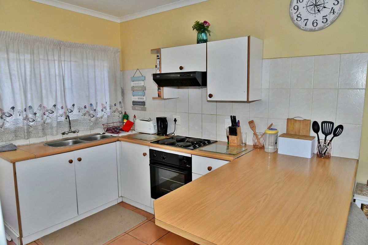 A functional kitchen featuring white cabinetry, wood-look laminate countertops, a built-in oven, electric hob, extractor fan, and a double stainless steel sink.