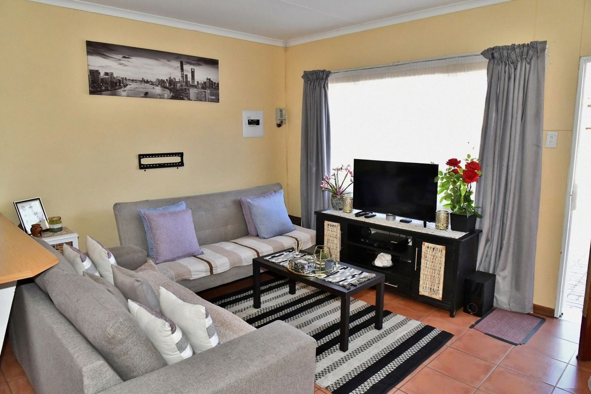 A cozy living room featuring tiled flooring, large windows with curtains, and neutral wall finishes, providing a comfortable and functional space.
