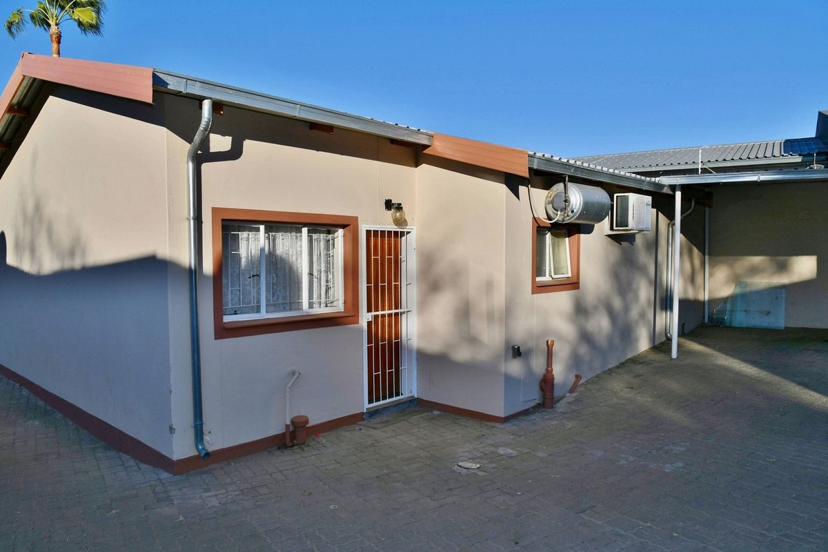Rear exterior view of the townhouse featuring paved courtyard area, security gate, and external wall-mounted water heater unit.