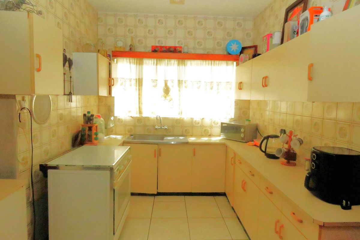 A dated kitchen featuring original cabinetry, tiled walls, and a functional layout with a window providing natural light.