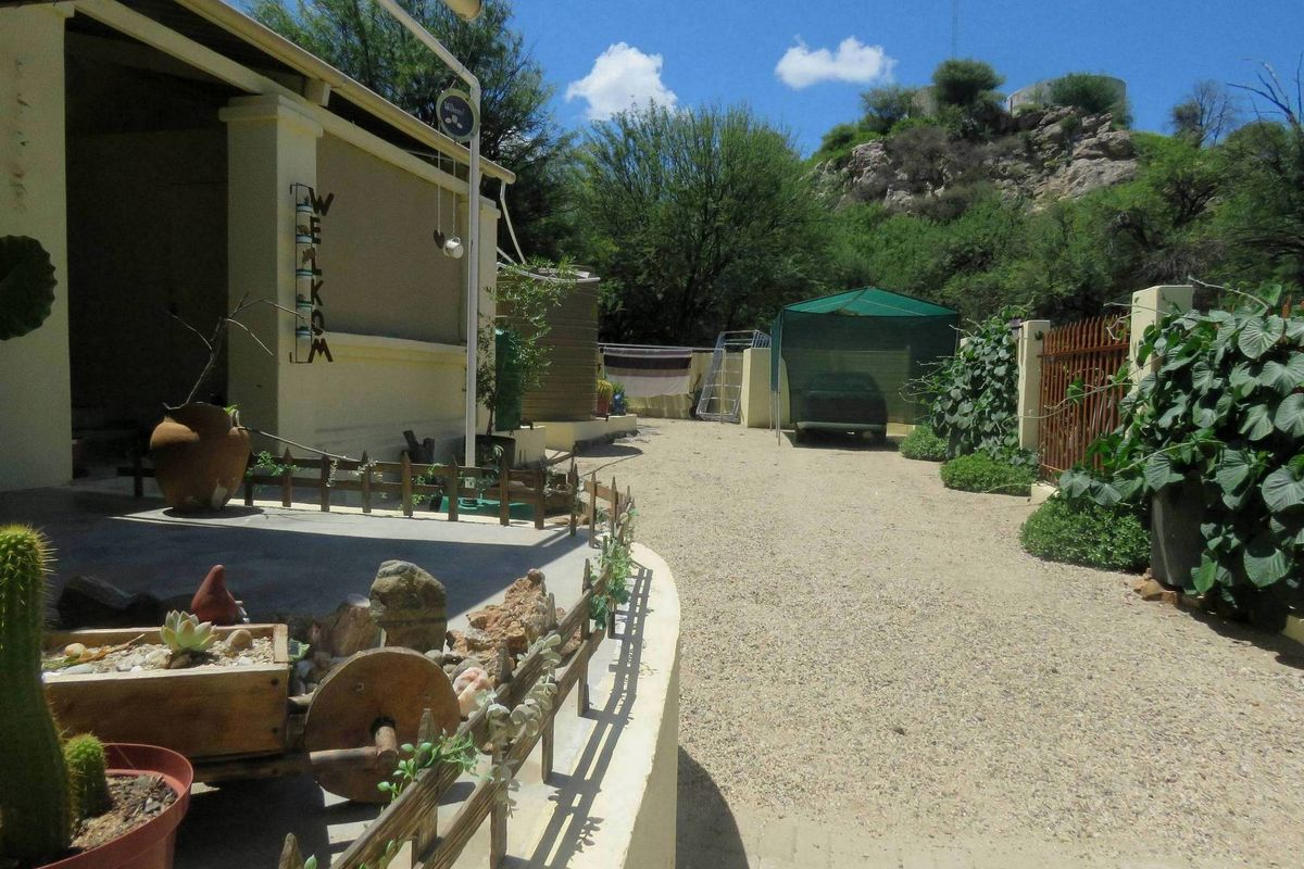 A view of the rear exterior area featuring a gravel driveway, a covered patio space, and a fenced garden boundary.