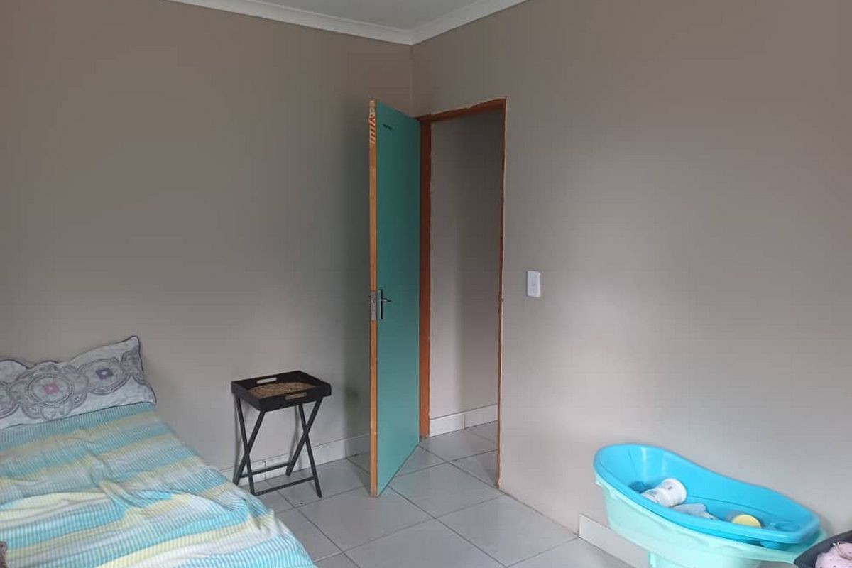 A simple bedroom featuring neutral wall paint, tiled flooring, and a doorway leading to an adjacent space.
