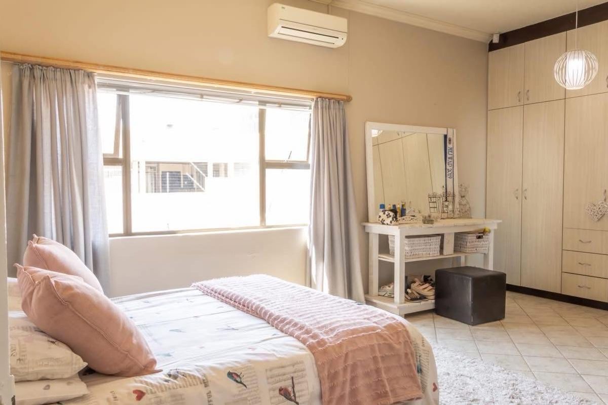 A well-maintained bedroom featuring built-in cupboards, tiled flooring, and a wall-mounted split-system air conditioner.
