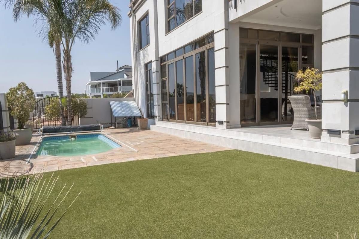 Rear exterior view featuring a swimming pool, artificial lawn, tiled patio area, and large aluminium sliding doors leading into the home.
