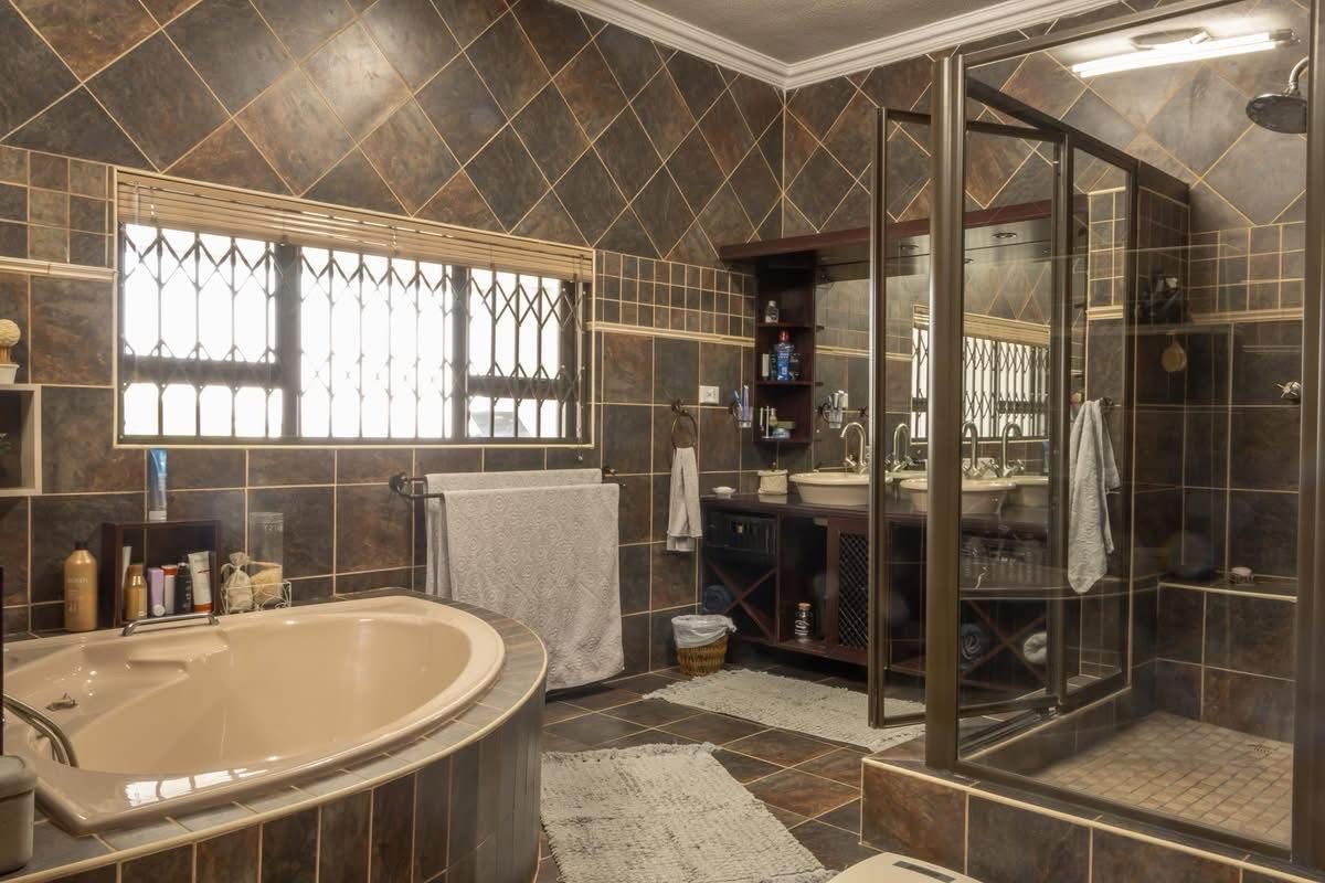 A spacious bathroom featuring dark tiled walls, a corner soaking tub, a glass-enclosed shower, and a built-in vanity with dual vessel sinks.
