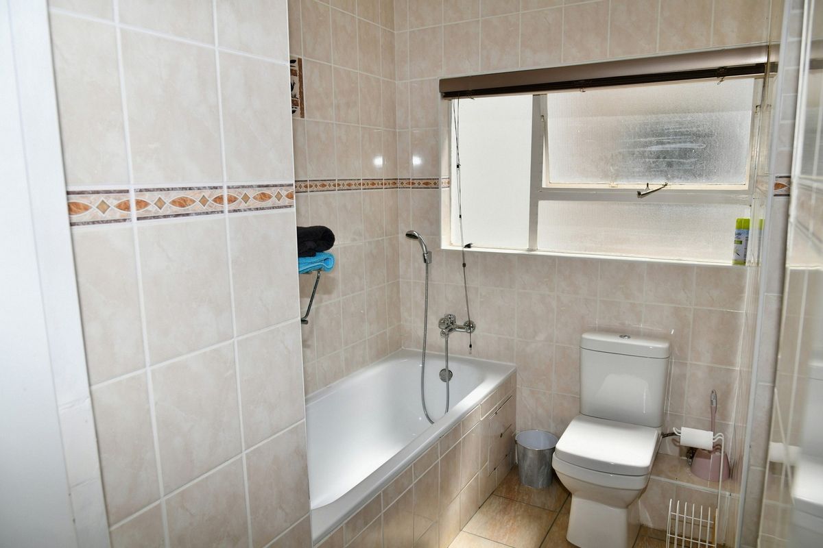 A functional bathroom featuring a built-in bathtub with a handheld shower attachment, a standard toilet, and neutral wall tiling throughout.