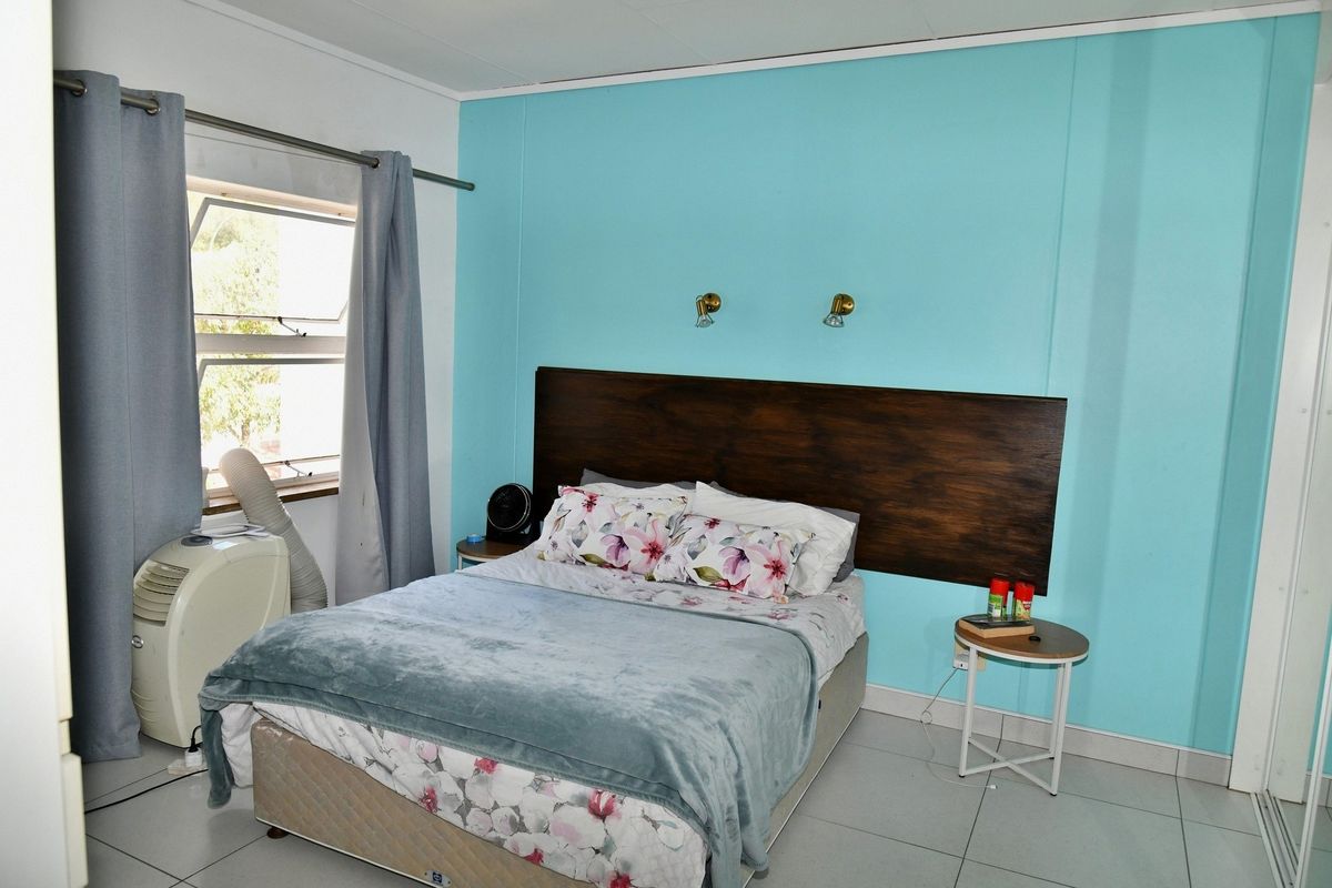 A bedroom featuring tiled flooring, a built-in dark wood headboard, and wall-mounted accent lighting against a bright blue feature wall.