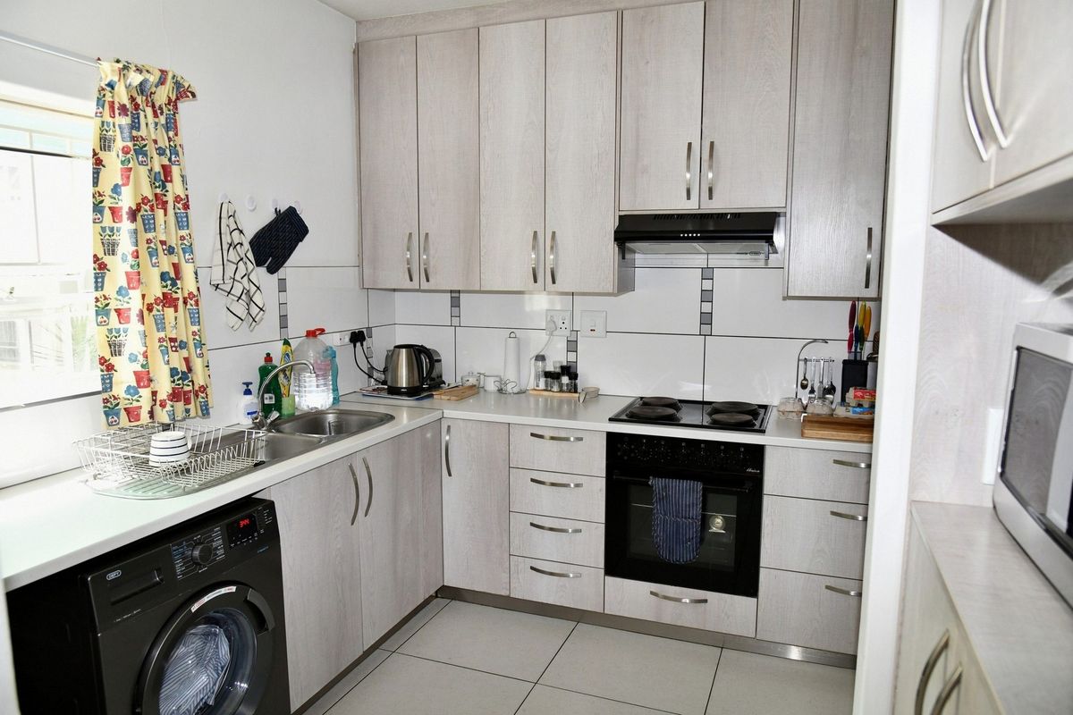 Compact kitchen featuring light wood-grain cabinetry, tiled backsplash, built-in oven, electric hob, extractor fan, and integrated laundry plumbing.