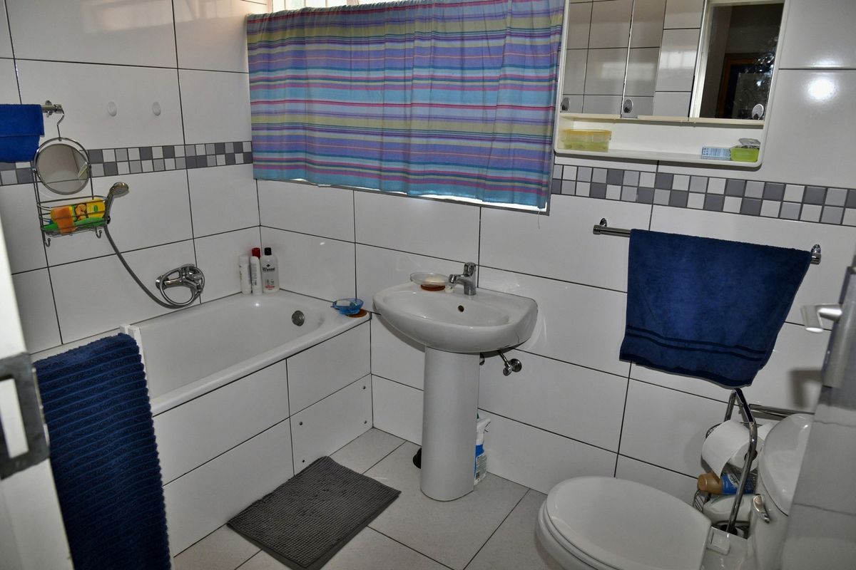 A functional bathroom featuring a white pedestal basin, a bathtub with shower mixer, and tiled walls with a decorative mosaic border.