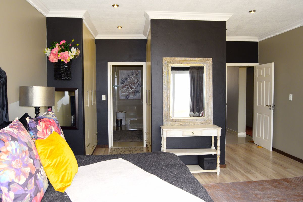 Spacious bedroom featuring built-in cupboards, recessed downlighting, crown molding, and laminate flooring, with direct access to an en-suite bathroom.