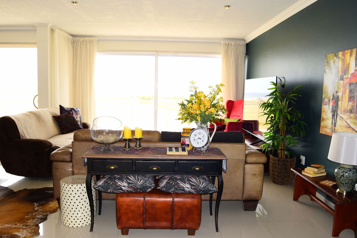 A bright and spacious living room featuring large sliding glass doors, polished tiled flooring, and recessed downlighting with a modern dark accent wall.
