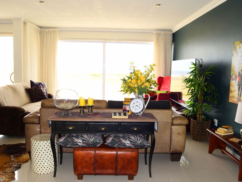 A bright and spacious living room featuring large sliding glass doors, polished tiled flooring, and recessed downlighting with a modern dark accent wall.