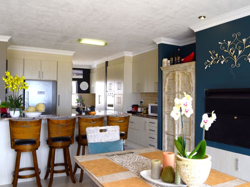 An open-plan kitchen and dining area featuring light-toned cabinetry, stone countertops, and a striking dark blue accent wall with decorative wall art.