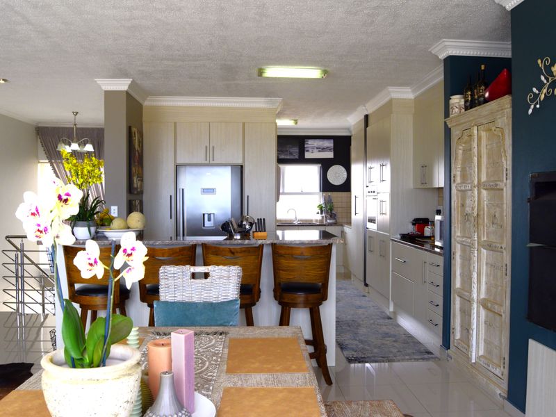 Spacious open-plan kitchen and dining area featuring modern built-in cabinetry, stone countertops, integrated appliances, and a functional breakfast bar with tiled flooring.