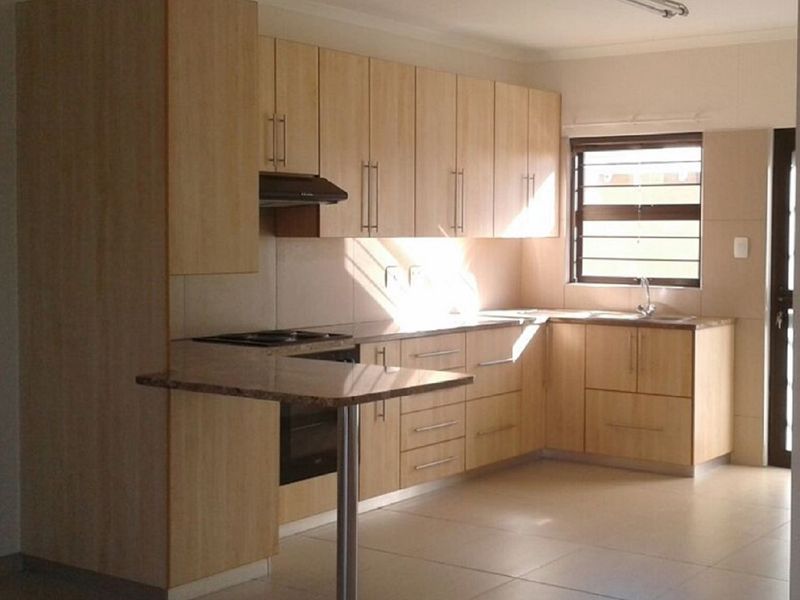 A functional kitchen featuring light wood cabinetry, granite countertops, a built-in oven, hob, extractor fan, and tiled flooring.