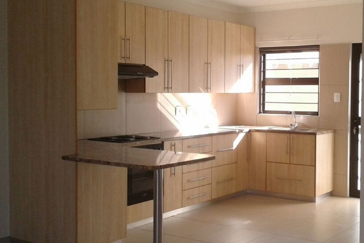 A functional kitchen featuring light wood cabinetry, granite countertops, a built-in oven, hob, extractor fan, and tiled flooring.