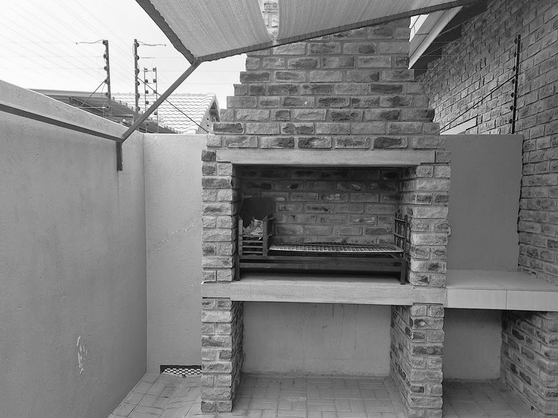 Outdoor patio area featuring a built-in brick braai or barbecue fireplace, paved flooring, and a shade sail structure for sun protection.