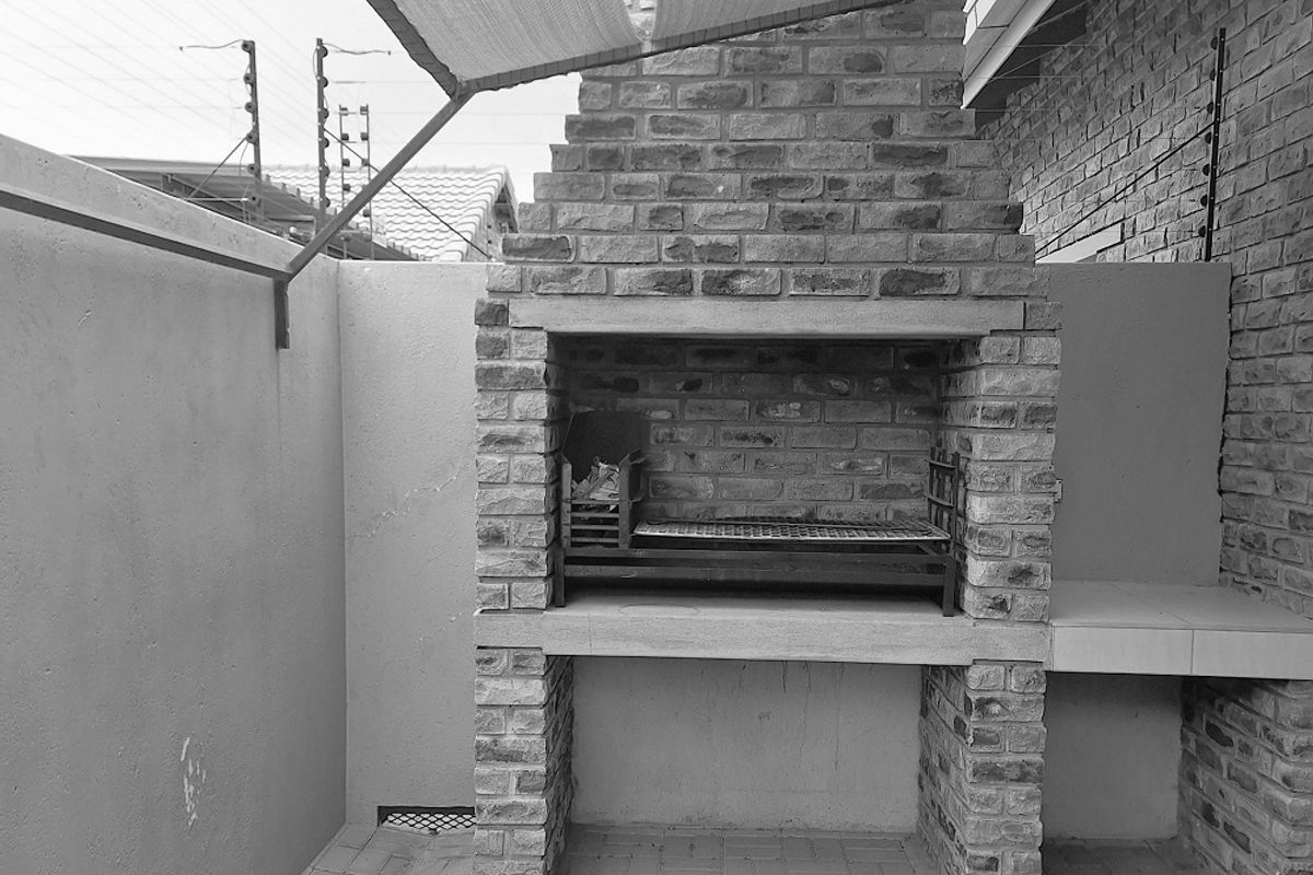 Outdoor patio area featuring a built-in brick braai or barbecue fireplace, paved flooring, and a shade sail structure for sun protection.
