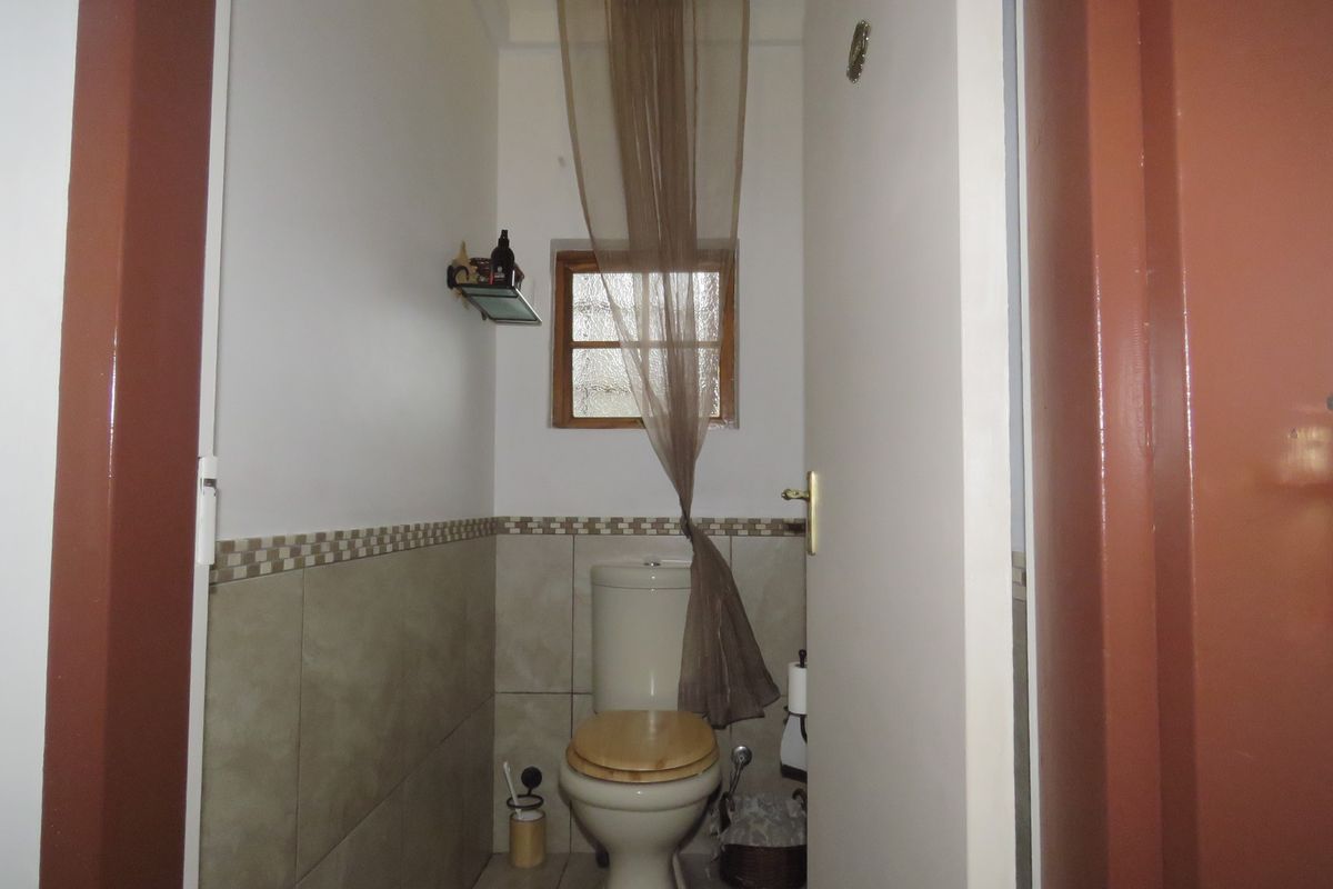 A compact bathroom featuring a standard toilet, tiled wall accents, and a small window, providing functional utility in a modest space.