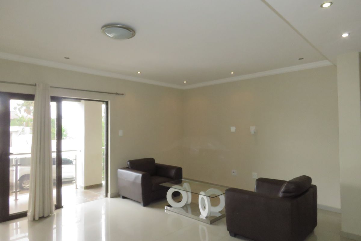 A bright, open-plan living area featuring neutral tiled floors, recessed ceiling lighting, and a sliding glass door leading to an outdoor patio.