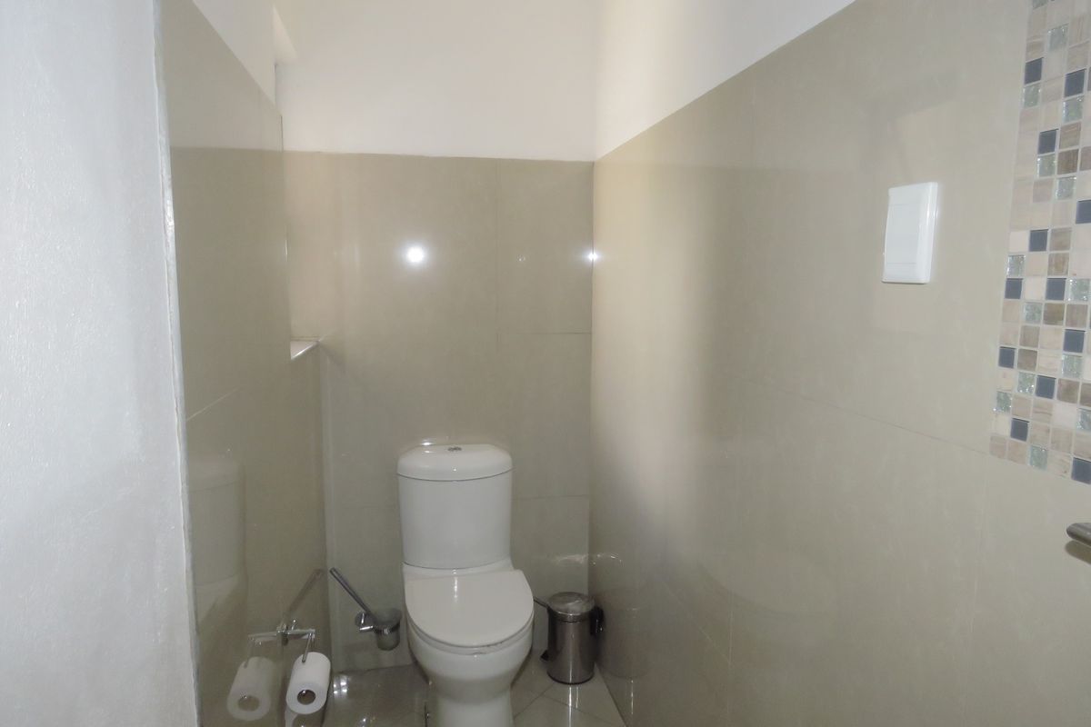 A compact bathroom featuring neutral ceramic wall tiles, a mosaic accent strip, and a standard white toilet.