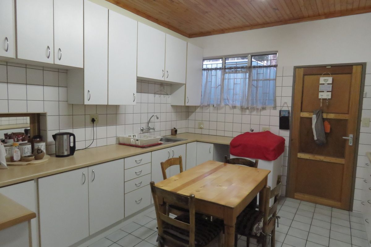 A functional kitchen featuring white cabinetry, tiled splashbacks, tiled flooring, and a timber ceiling, providing a practical workspace with an integrated dining area.