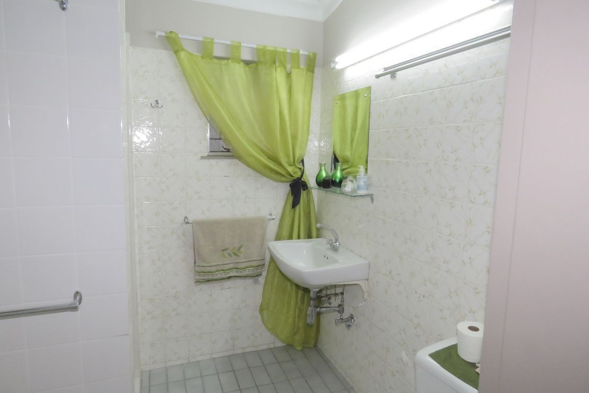 A functional bathroom featuring a wall-mounted basin, tiled walls, and a shower area with grab rails.