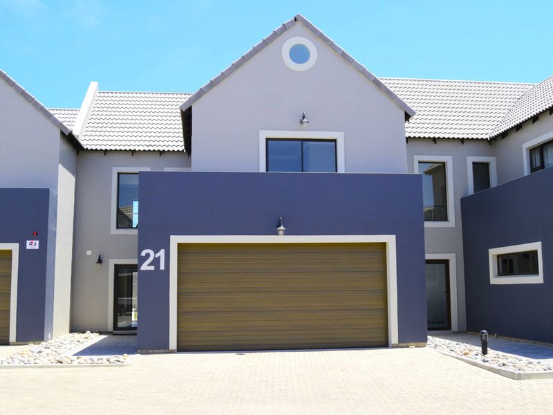 Front elevation of a modern townhouse featuring a paved driveway, integrated garage, and contemporary grey and blue facade finishes.
