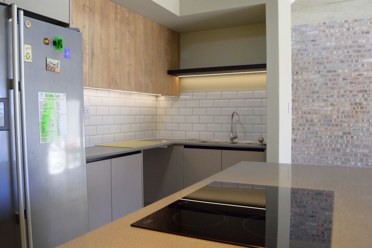 Modern kitchen featuring wood-look cabinetry, subway tile backsplash, stone countertops, integrated hob, and a striking exposed brick feature wall.