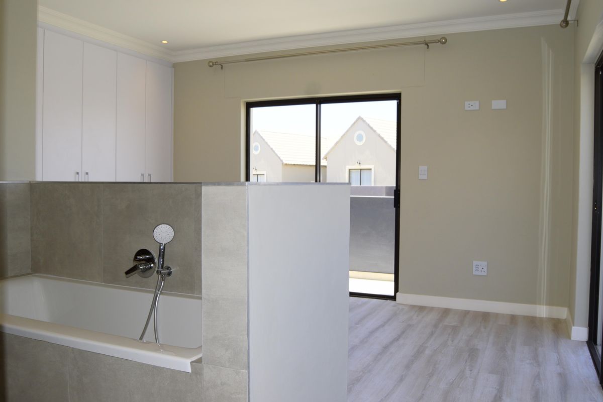 Spacious bedroom featuring an open-plan en-suite bathtub, built-in cupboards, modern laminate flooring, and a sliding door leading to a private balcony.