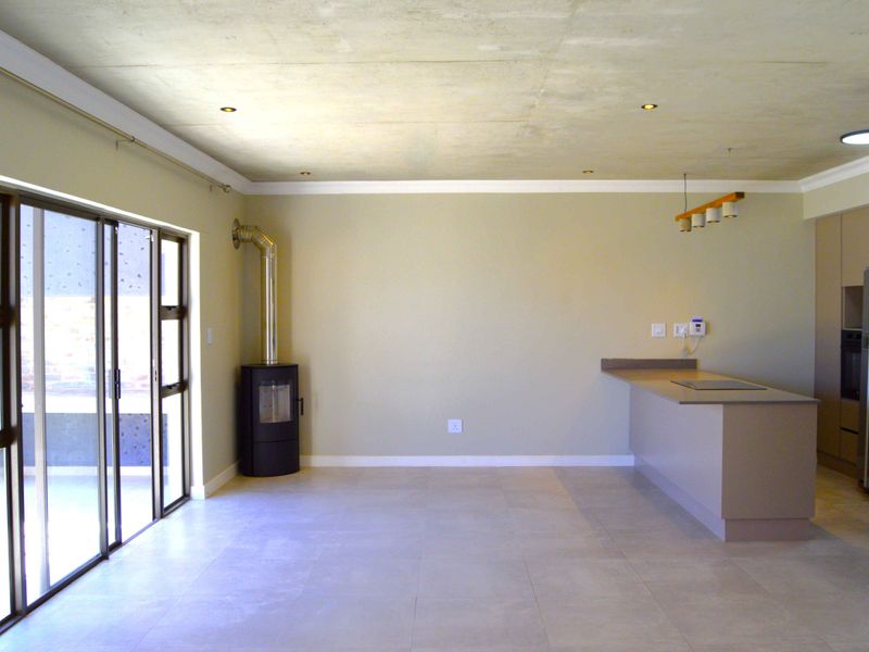 Spacious open-plan living and kitchen area featuring a modern freestanding fireplace, tiled flooring, and large sliding doors leading to the outdoor space.