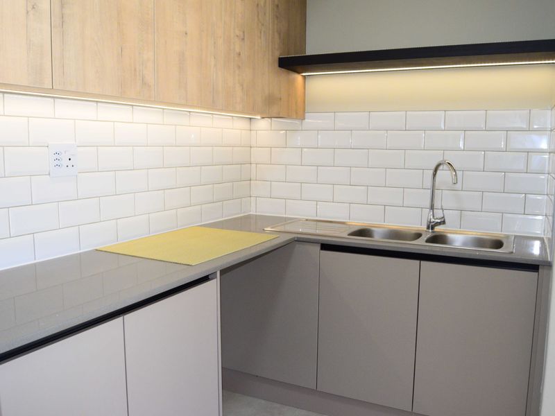 Modern kitchen featuring light wood-tone upper cabinets, grey lower cabinetry, quartz countertops, subway tile backsplash, and integrated under-cabinet lighting.
