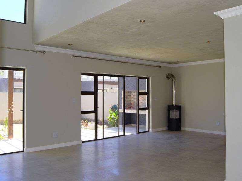 Spacious, light-filled living area featuring a modern freestanding fireplace, tiled floors, and large sliding doors opening to an outdoor patio area.