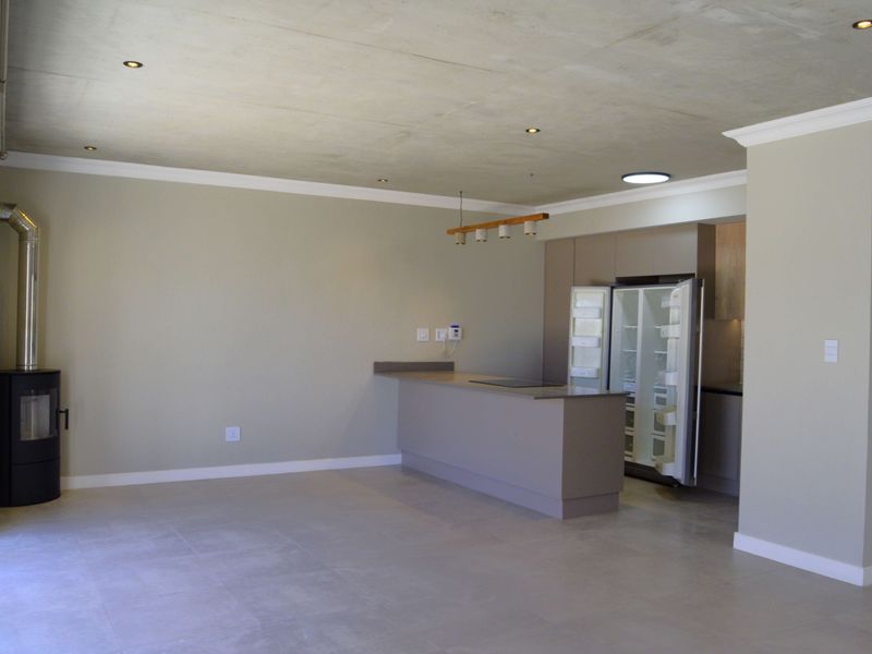 Spacious open-plan living and kitchen area featuring a modern freestanding fireplace, neutral tiled flooring, recessed lighting, and contemporary built-in kitchen cabinetry.