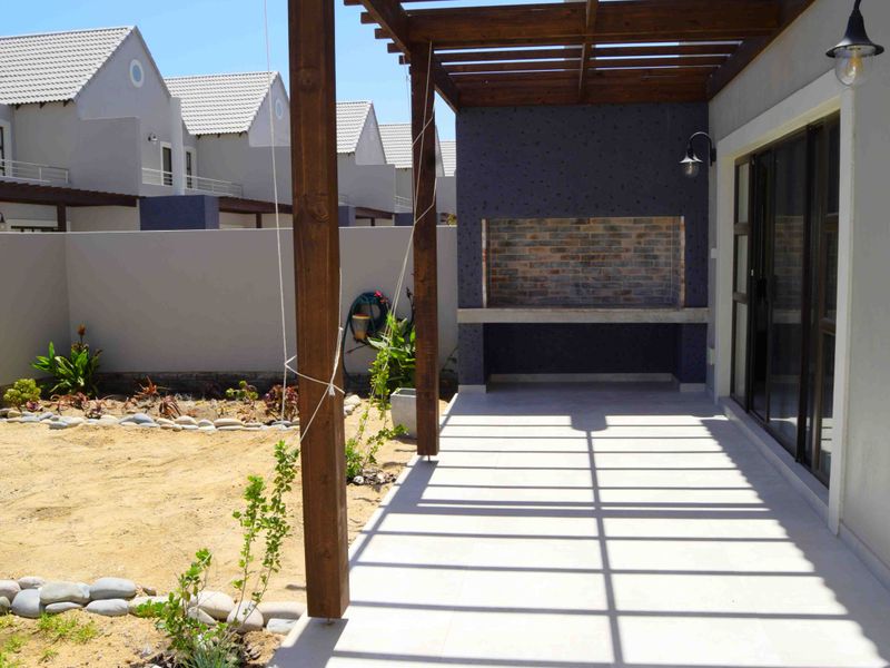 Covered patio area featuring a timber pergola, built-in brick braai with concrete counter, and direct access to the garden through sliding glass doors.