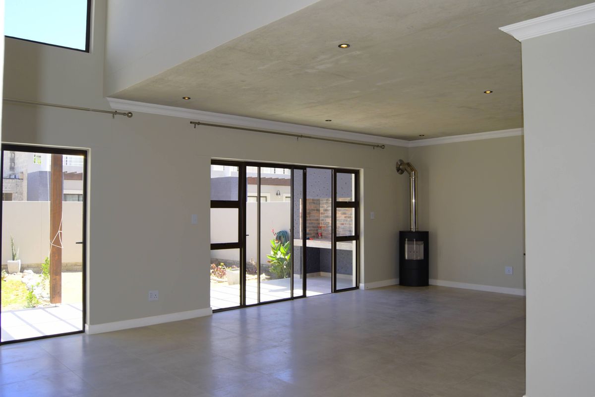 Spacious, light-filled living area featuring tiled floors, a modern freestanding fireplace, and large sliding doors opening to an outdoor patio space.
