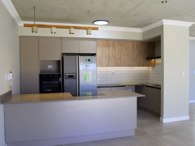 Modern kitchen featuring sleek cabinetry, stone countertops, subway tile backsplash, integrated hob and oven, and stylish pendant lighting in an open-plan layout.