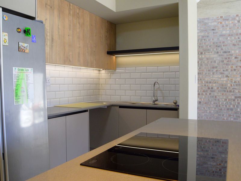 Modern kitchen featuring wood-tone and grey cabinetry, subway tile backsplash, stone countertops, integrated induction hob, and a stylish exposed brick feature wall.