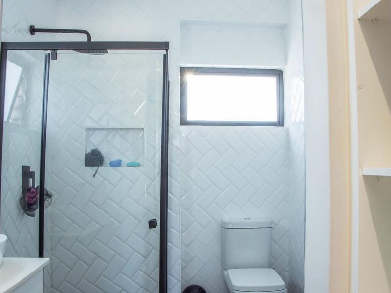 Modern bathroom featuring a glass shower enclosure with black framing, stylish white herringbone wall tiles, a built-in shower niche, and a toilet.
