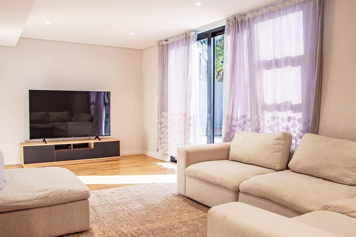 A bright and modern living room featuring hardwood flooring, recessed downlights, and large sliding glass doors that provide ample natural light.