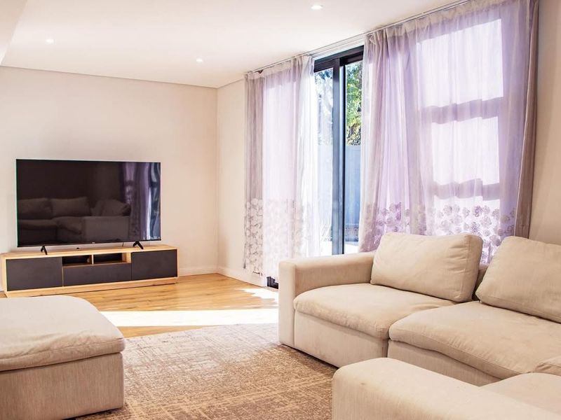 A bright and modern living room featuring hardwood flooring, recessed downlights, and large sliding glass doors that provide ample natural light.