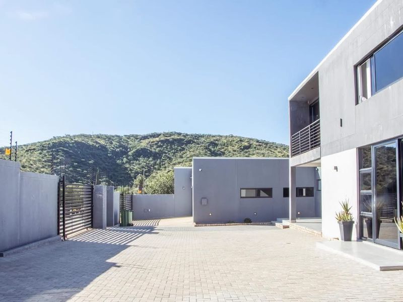 Modern two-story residence featuring a paved driveway, secure boundary wall with electric fencing, and contemporary architectural design with mountain views.