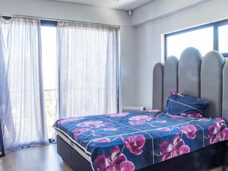 A bright and modern bedroom featuring laminate flooring, large windows, and sliding glass doors that provide ample natural light.