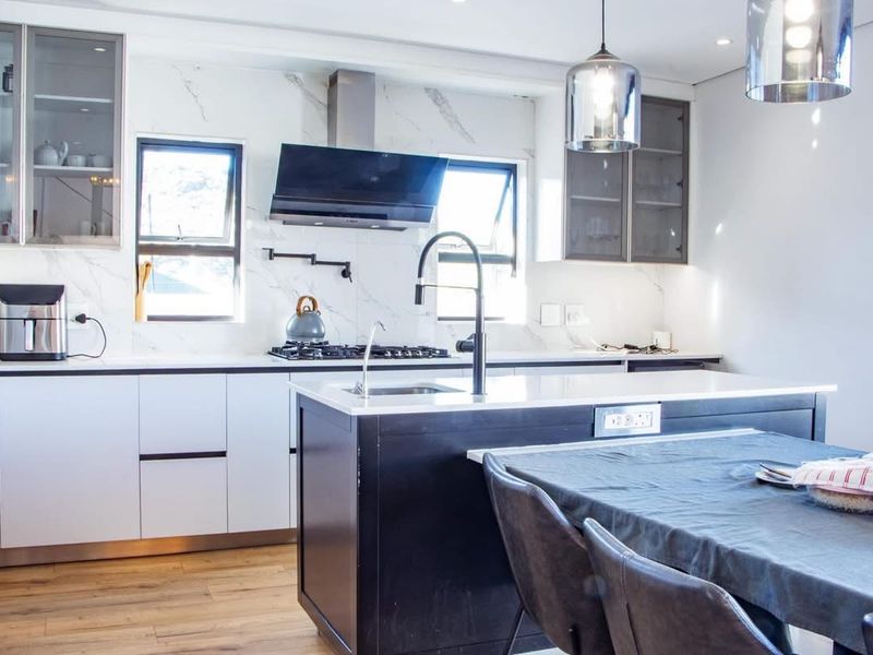 Modern kitchen featuring a central island, marble-look splashback, gas hob, extractor fan, and high-quality cabinetry with integrated lighting.
