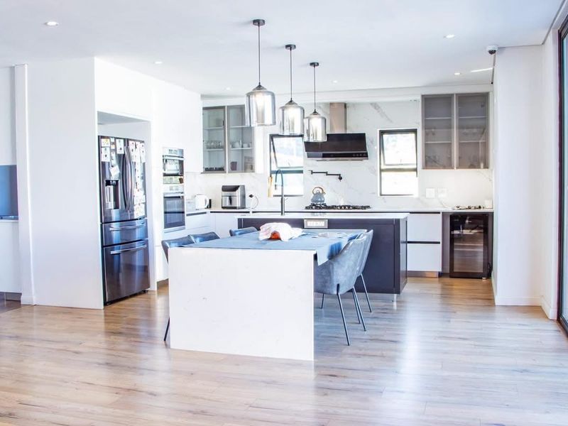 Modern open-plan kitchen featuring a central island, stone countertops, integrated appliances, and sleek cabinetry with contemporary pendant lighting.