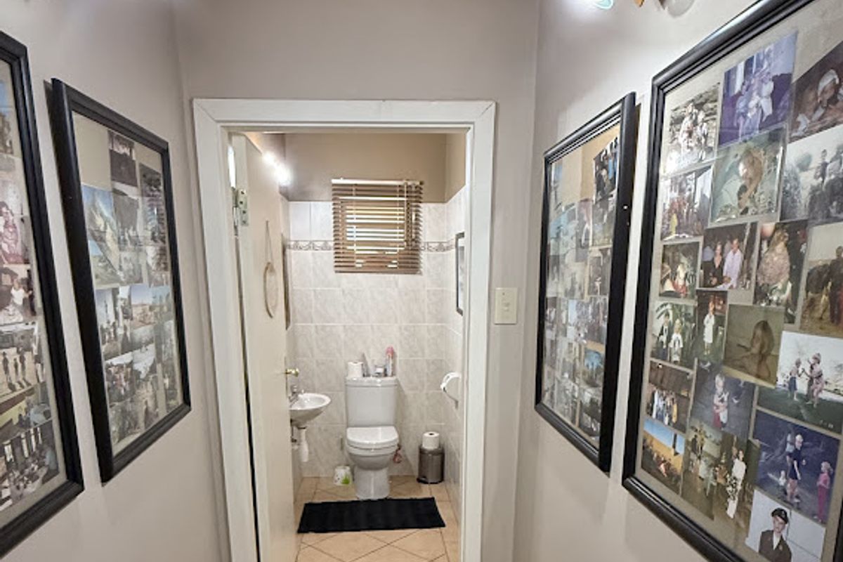 A compact bathroom featuring a wall-mounted basin, close-coupled toilet, and neutral wall tiling, accessed via a hallway.