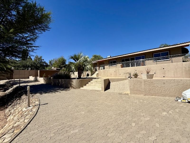 Front exterior view featuring a paved driveway, tiered retaining walls with stone accents, and a raised terrace with metal balustrades.