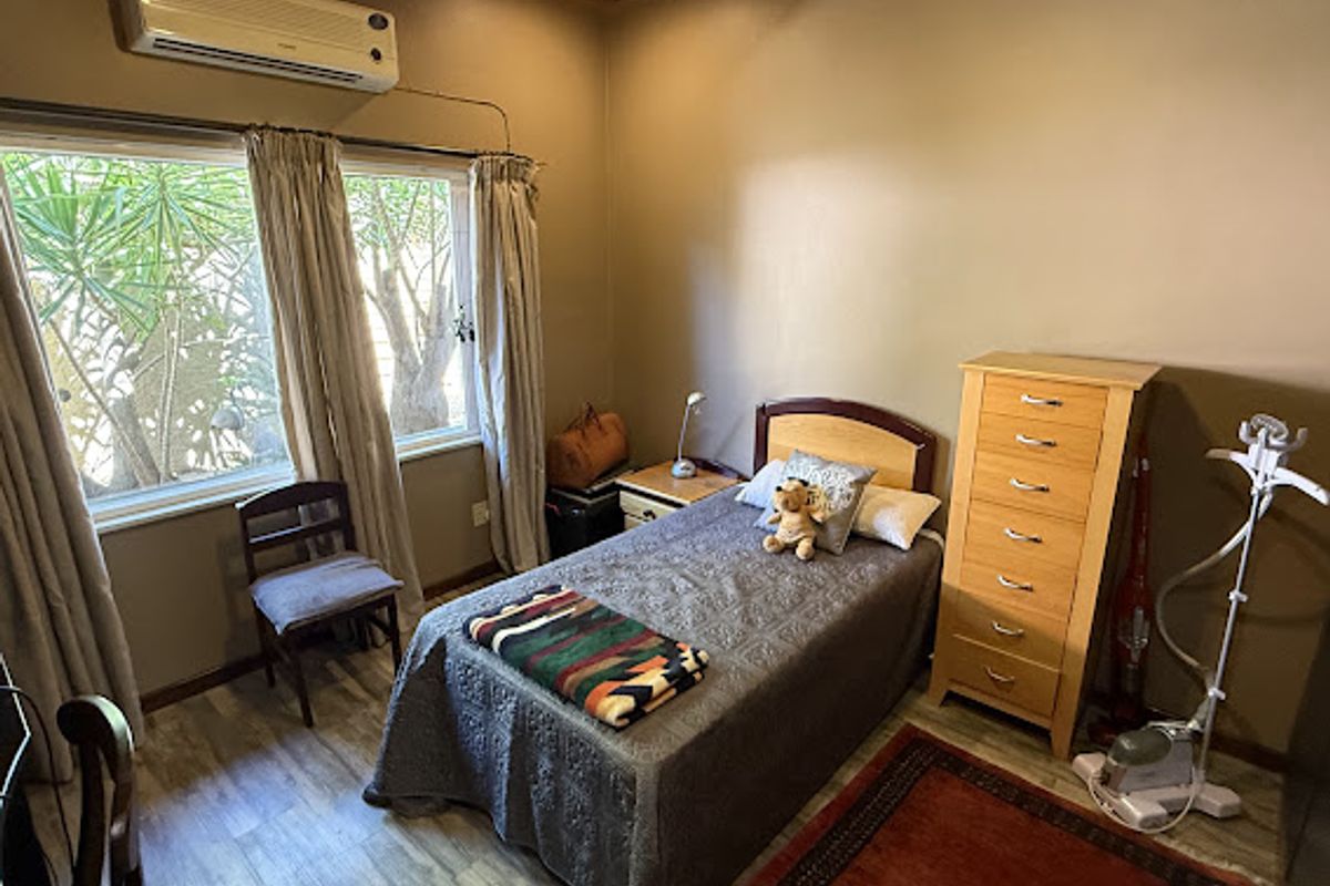 A cozy bedroom featuring laminate flooring, a timber ceiling, and a wall-mounted split-system air conditioner.
